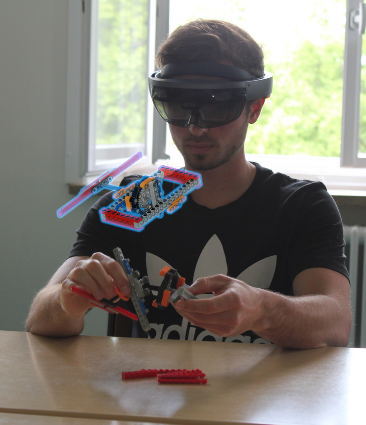Auf dem Bild ist ein junger Mann mit einer Datenbrille zu sehen. Dieser baut aus Legoteilen ein Planetengetriebe zusammen. Außerdem ist ein virtuelles Objekt des Planetengetriebe zu sehen.