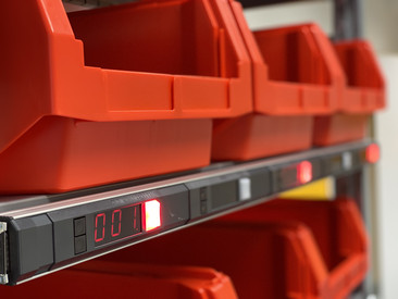 Zdjęcie przedstawia czerwony, otwarty pojemnik magazynowy z podświetlanym wyświetlaczem systemu pick-by-light.